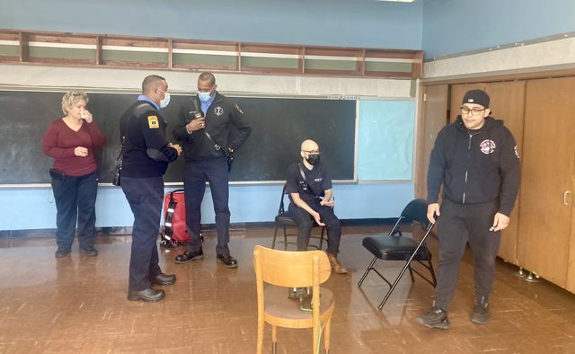 B-HEARD team members act out a scenario in which they're called to a dispute between a mother, far left, and her son, far right. The social worker is seated, and the EMTs are standing next to him.